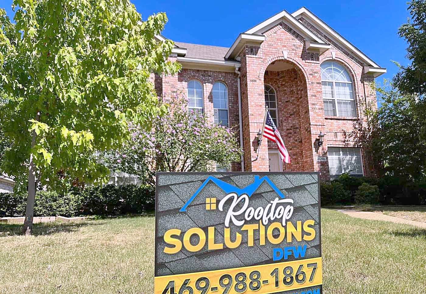 A Rooftop Solutions yard sign on the lawn of a two-story brick home